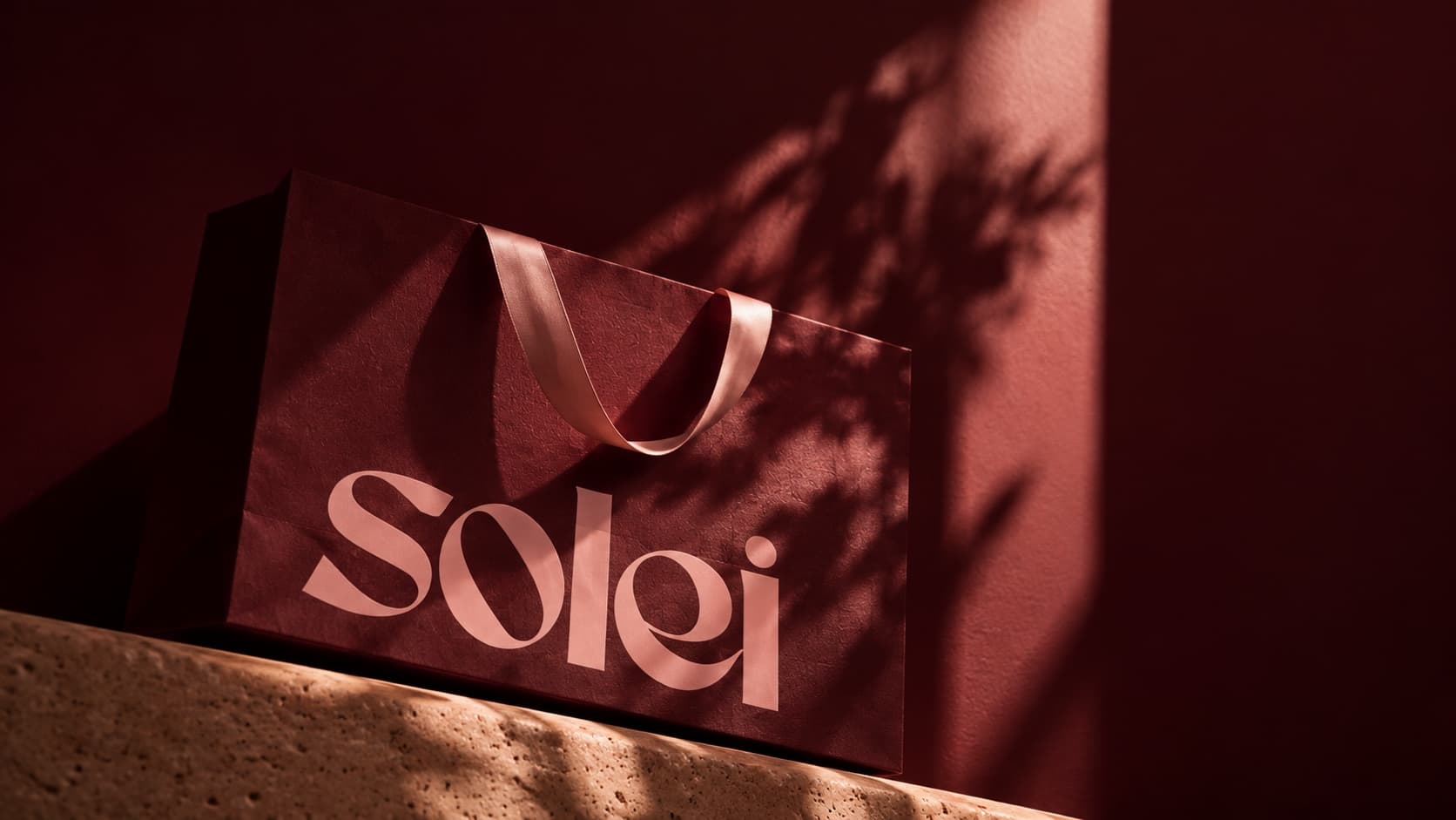 A burgundy Solei gift bag with a satin ribbon in late-afternoon light